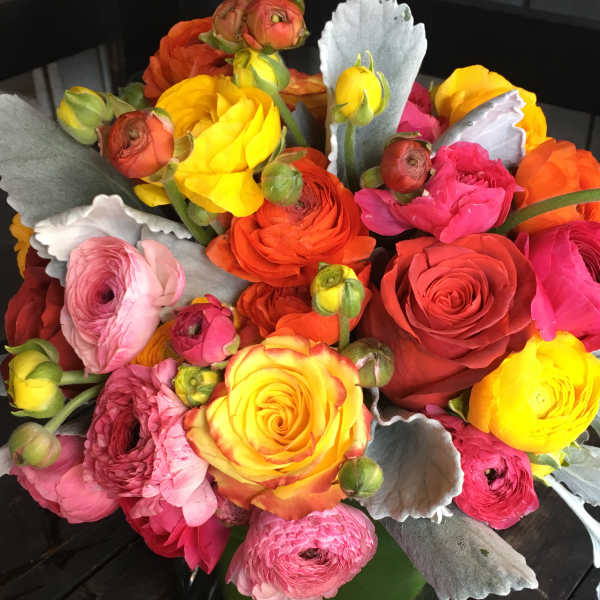 Bright mixed bouquet of ranunculus and roses in a glass vase