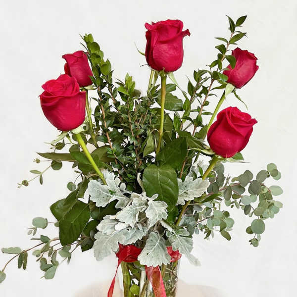 Five red roses in a clear glass vase with silver foliage and ribbon