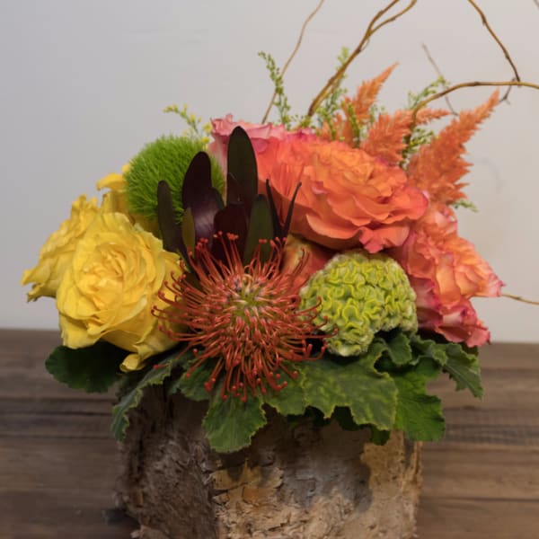 Mixed floral arrangement in a rustic bark container with yellow and orange blooms