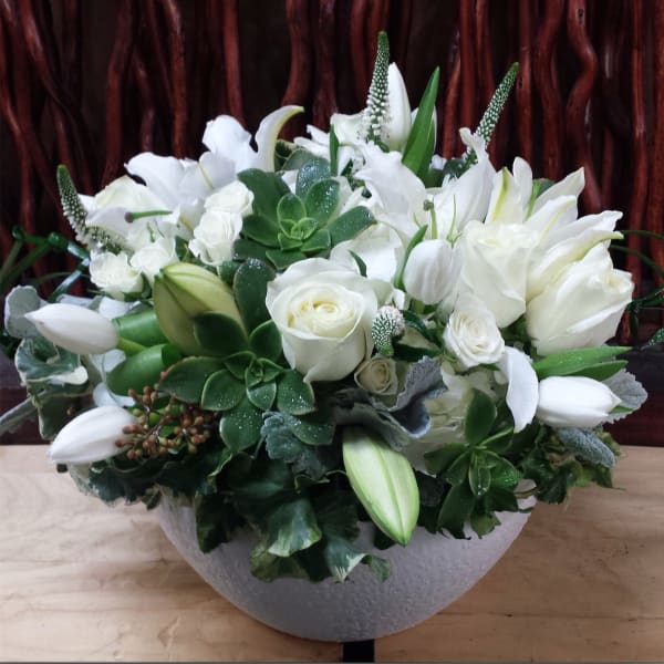 White floral arrangement in a round gray vase with roses and lilies