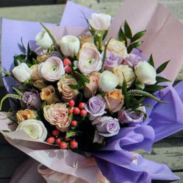 Pastel bouquet of roses and ranunculus wrapped in lavender paper