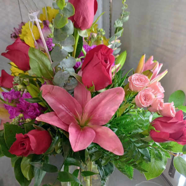 Mixed bouquet with pink lilies, red roses, and pink spray roses in a glass vase