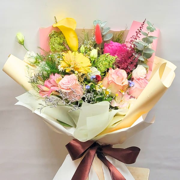 Mixed bouquet with pink and yellow flowers wrapped in cream paper