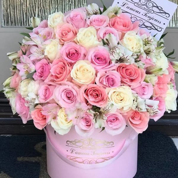 Large round arrangement of pink and cream roses with white accent flowers in a pale pink hat box.