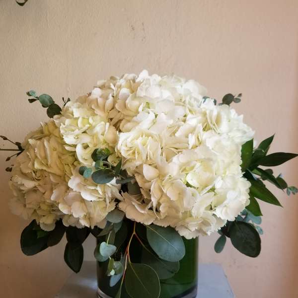White hydrangea bouquet in a green glass vase with eucalyptus