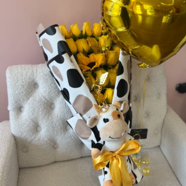 Bouquet of yellow roses and sunflowers with a plush cow and gold heart balloon on a chair