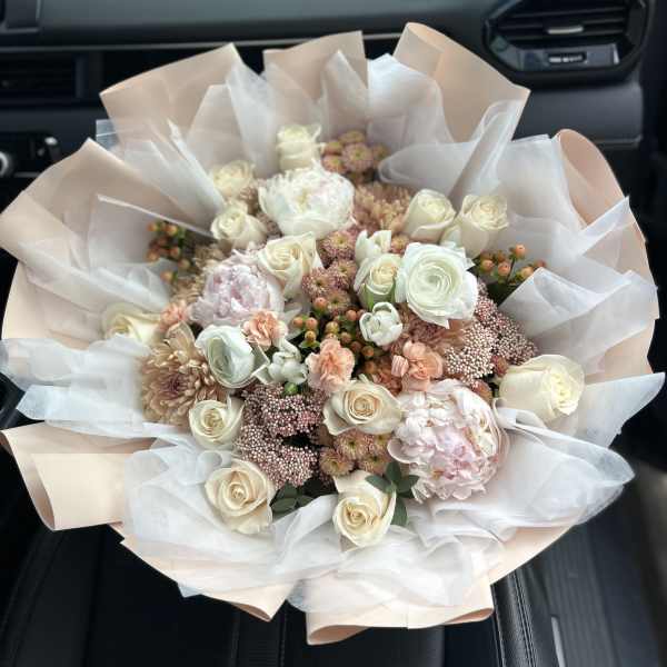 Bouquet of cream and blush roses with pale pink flowers wrapped in white paper