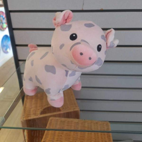 Small pink plush pig with gray spots displayed on a glass shelf.