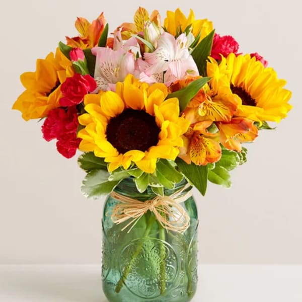 Bouquet of sunflowers, alstroemeria, and carnations in a green glass jar