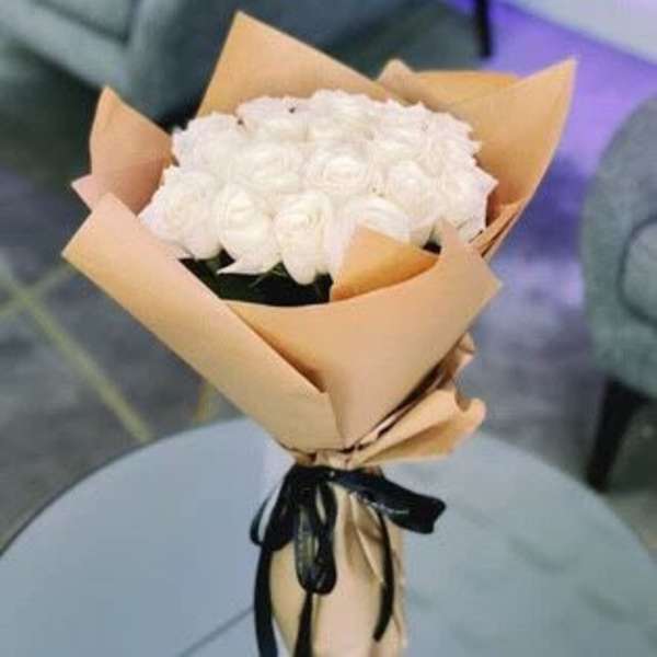 Bouquet of white roses wrapped in tan paper with a black ribbon