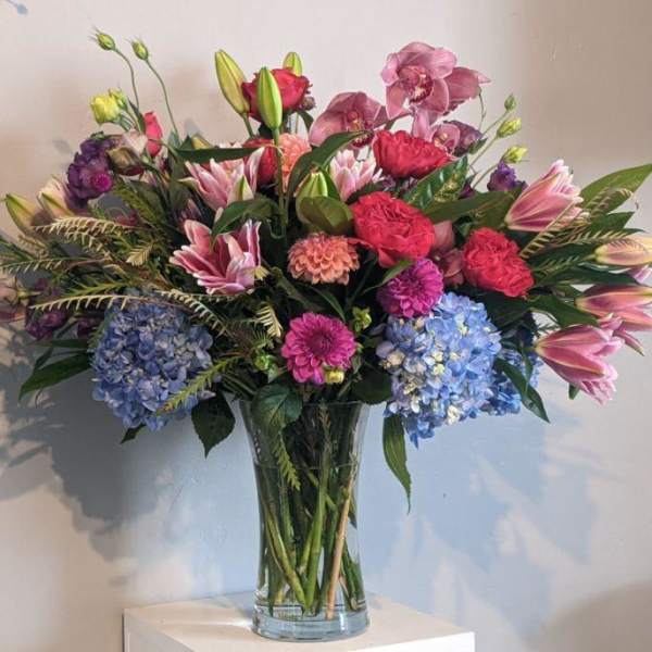 Mixed bouquet of pink, purple, and blue flowers in a clear glass vase
