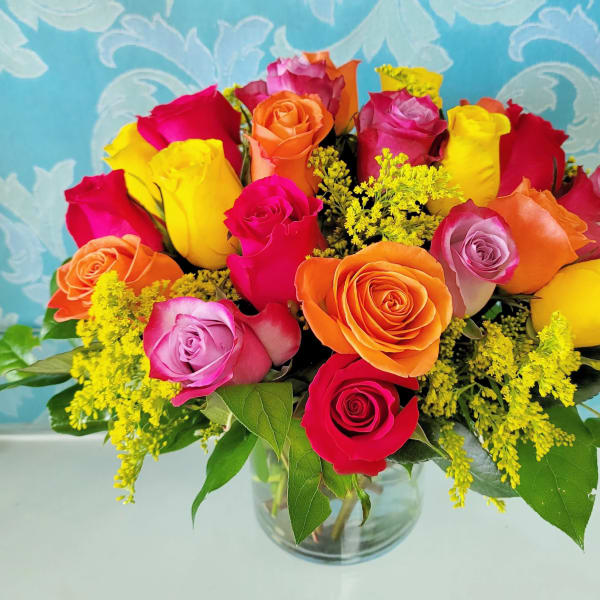 Vibrant bouquet of multicolored roses with yellow filler flowers in a clear glass vase