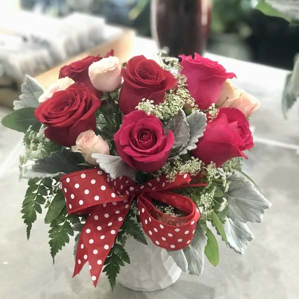 Bouquet of red and pink roses in a white vase with a red polka-dot ribbon