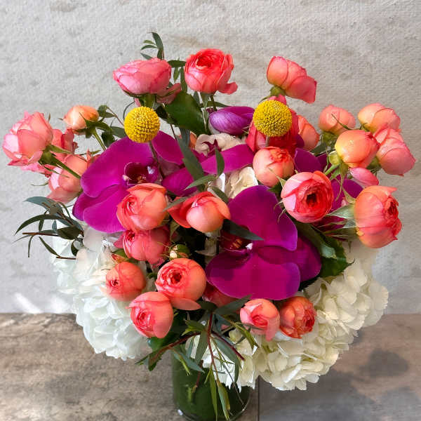 Bouquet of pink ranunculus, purple orchids, and white hydrangeas in a glass vase