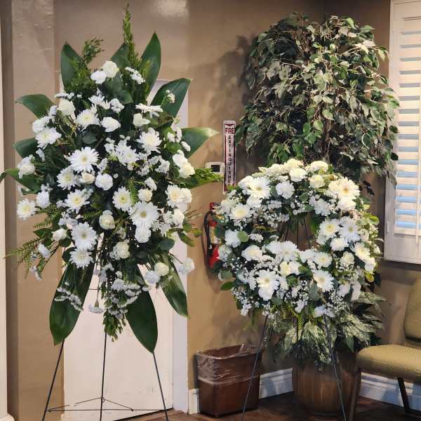Two white floral standing sprays on black easels in an indoor room.