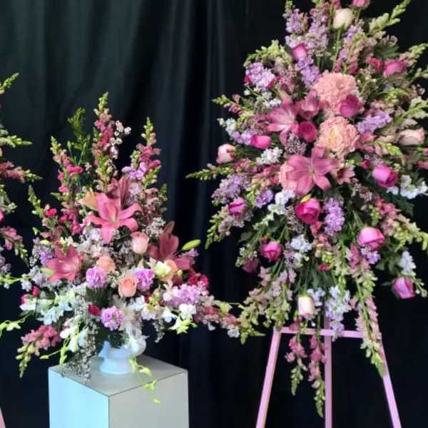 Three pink and lavender floral arrangements on stands and a pedestal