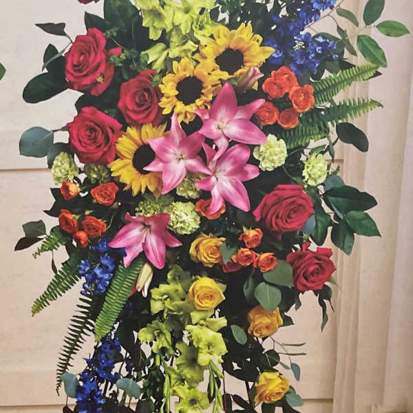 Tall standing floral spray with roses, lilies, sunflowers, and blue flowers