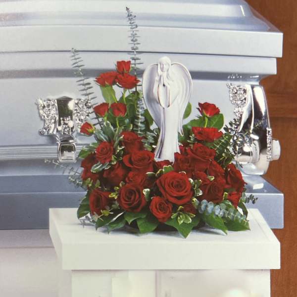 Red roses arranged around a white angel figurine on a casket