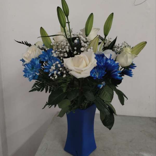 White roses, blue chrysanthemums, lilies, and baby's breath in a tall blue vase