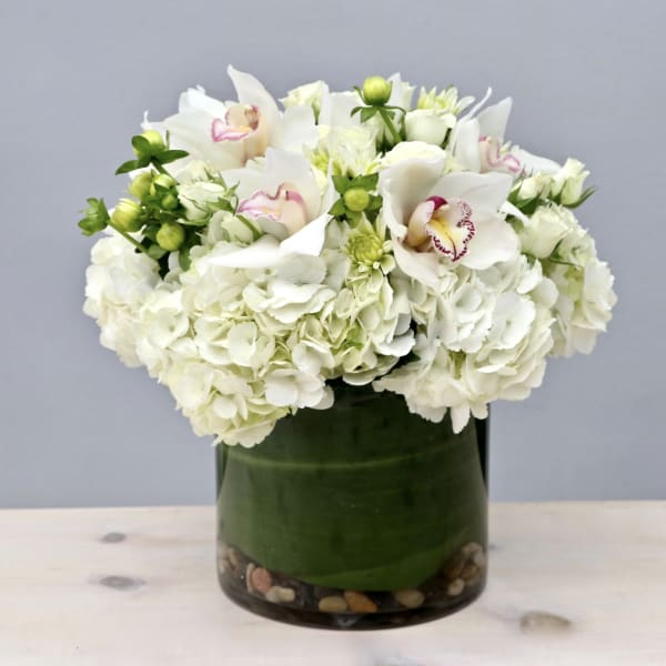 White hydrangeas and orchids in a green glass vase