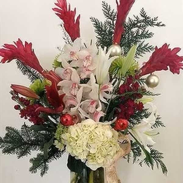Tall holiday bouquet with white orchids, red accents, and evergreen branches in a glass vase