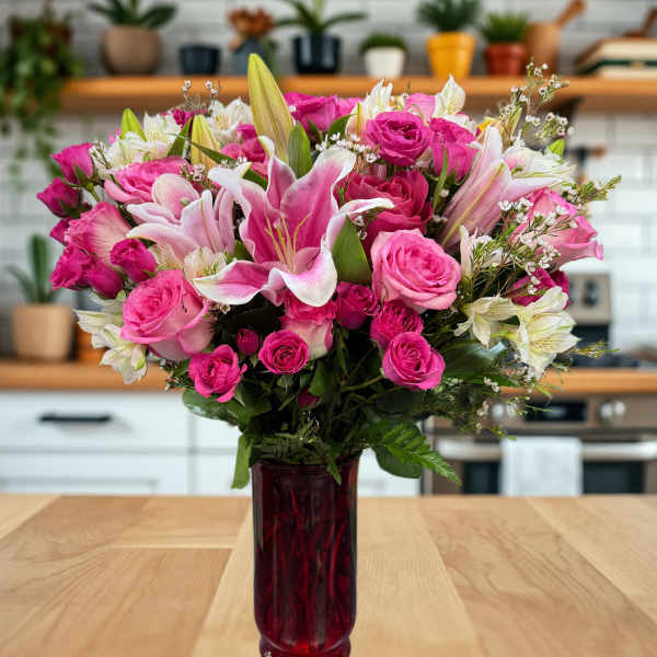 Pink roses and lilies arranged in a red glass vase
