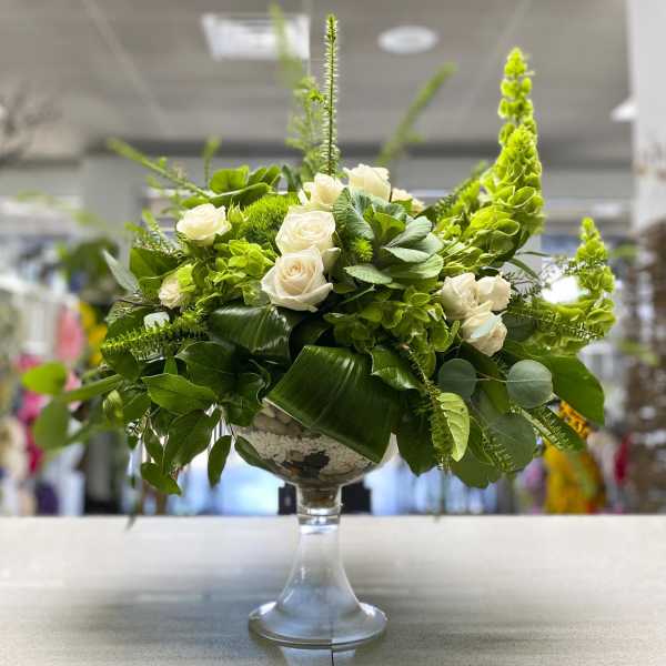 White roses and green flowers in a glass pedestal vase