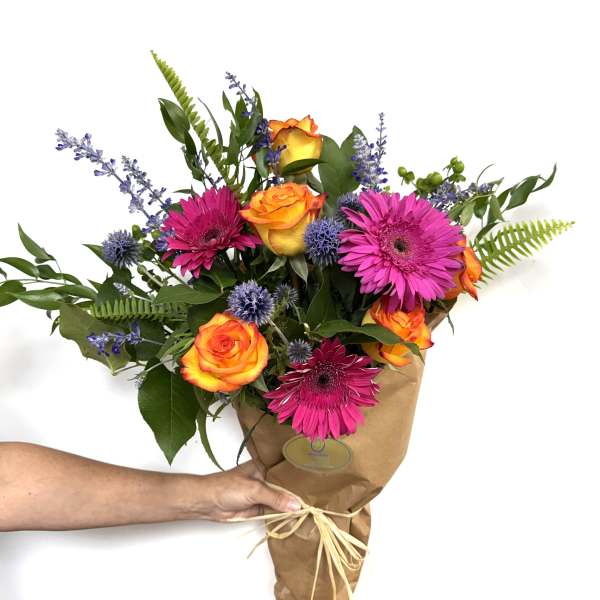 Bouquet of orange roses, pink gerberas, and purple accents in brown paper