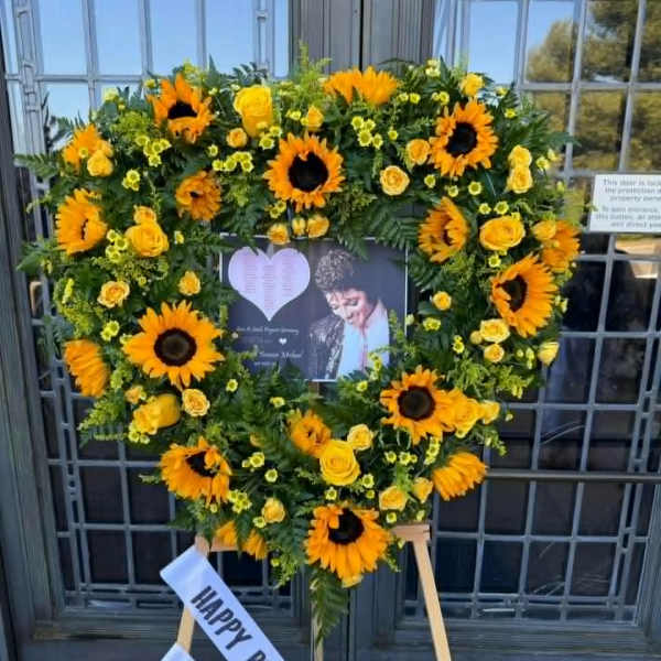Heart-shaped sunflower and yellow rose standing wreath on an easel with a birthday ribbon