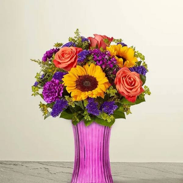 Bouquet of sunflowers, roses, and purple flowers in a pink vase