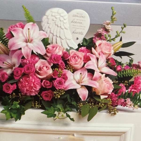 Pink lilies and roses arranged with angel wings and a heart plaque