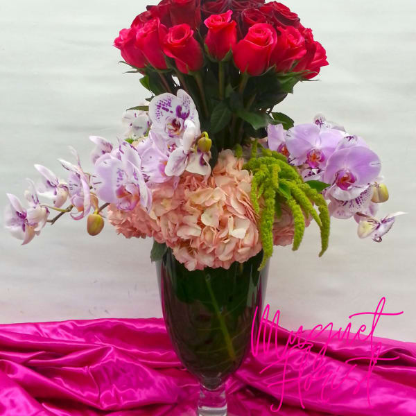 Bouquet of red roses and pale orchids in a tall glass vase