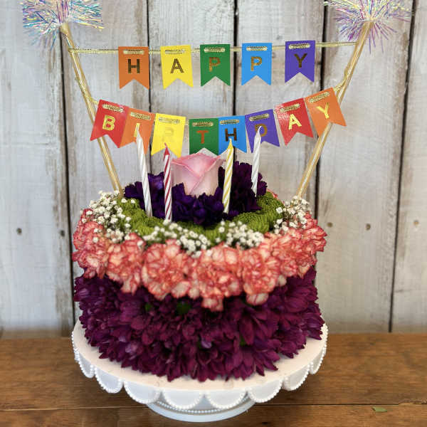 Birthday cake decorated with flowers and a colorful HAPPY BIRTHDAY banner
