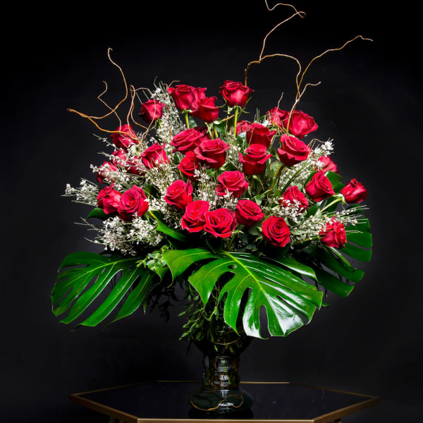 Large bouquet of red roses in a glass vase with tropical leaves