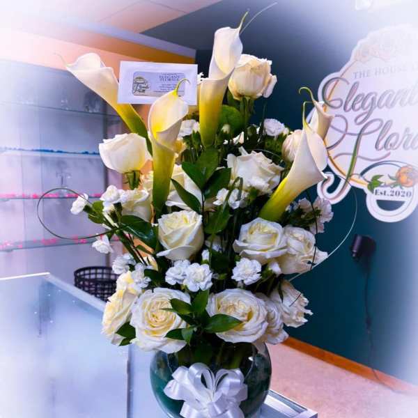White calla lilies and roses arranged in a glass vase with a white ribbon