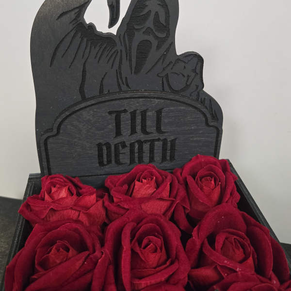 Red roses arranged below a black "Till Death" grave marker
