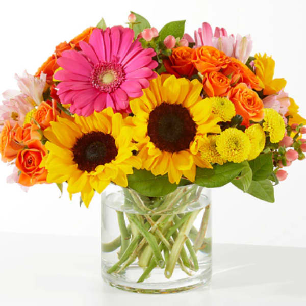 Bright mixed bouquet with sunflowers, roses, and a pink gerbera in a glass vase