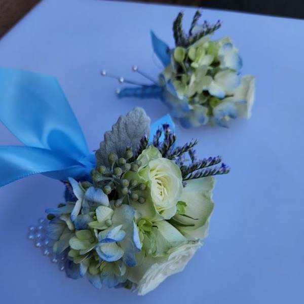 Blue and white wrist corsages with roses and hydrangea, accented with ribbon and pearls on a light background