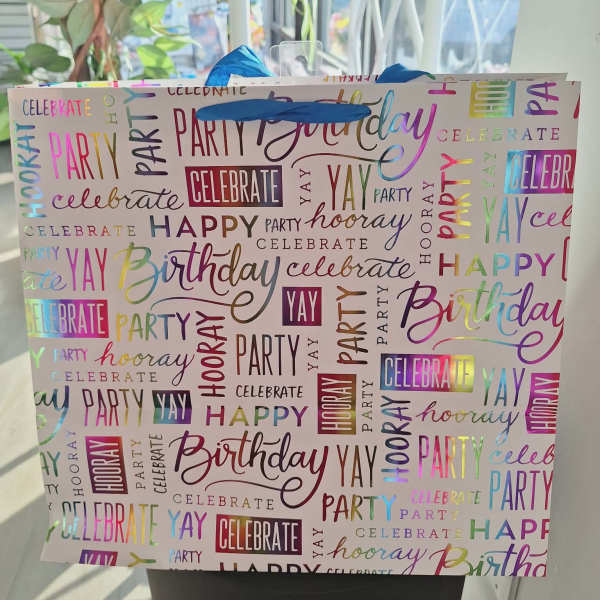 Birthday gift bag with colorful party words and blue tissue paper