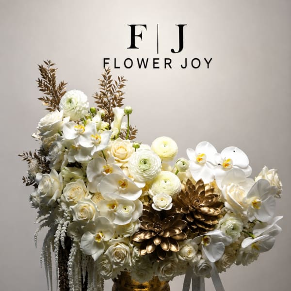 White floral arrangement in a gold urn with ribbon accents