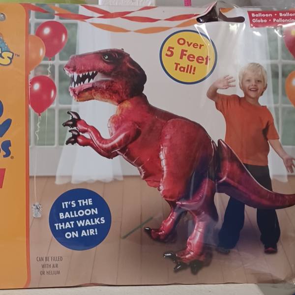 Package for a red dinosaur foil balloon with a child pictured beside it.