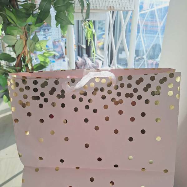 Pink gift bag with gold polka dots and white ribbon handles