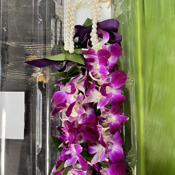 Purple orchid lei with pearl beads and ribbon in clear packaging