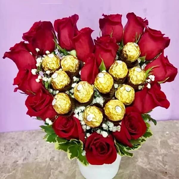 Heart-shaped bouquet of red roses with gold-wrapped chocolates in a white vase
