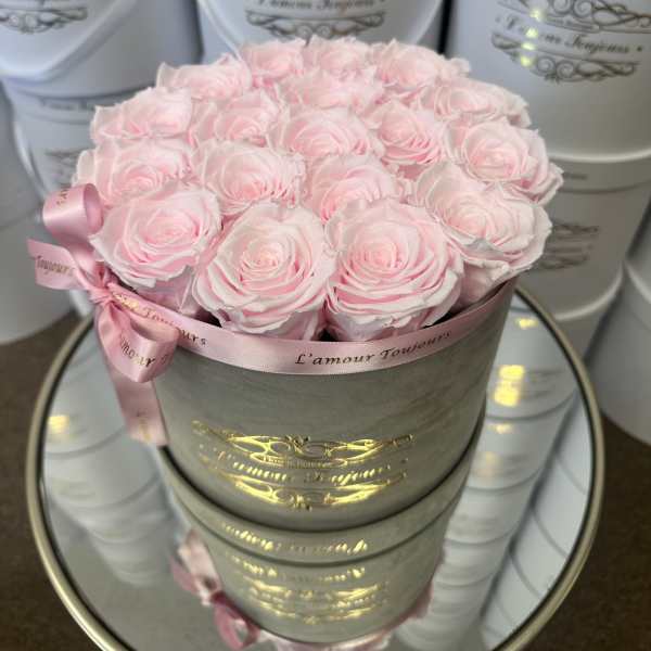 Round gray hat box filled with tightly packed light pink roses and tied with a pink ribbon.