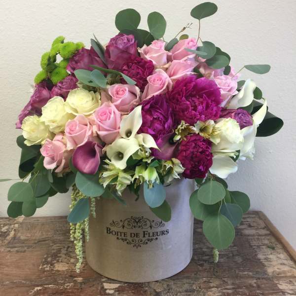 Mixed pink and white flowers arranged in a round box with greenery