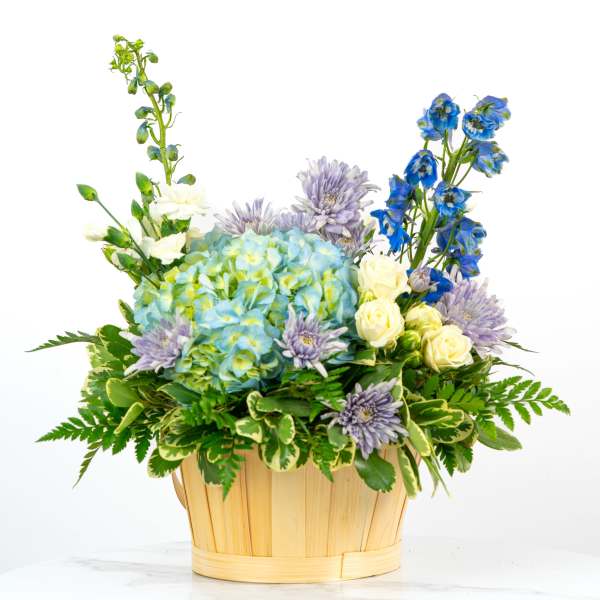 Basket arrangement with blue hydrangeas, white roses, lavender mums, and blue delphinium