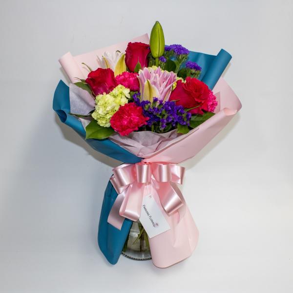Mixed bouquet of roses, lilies, carnations, and purple filler flowers wrapped in pink and blue paper