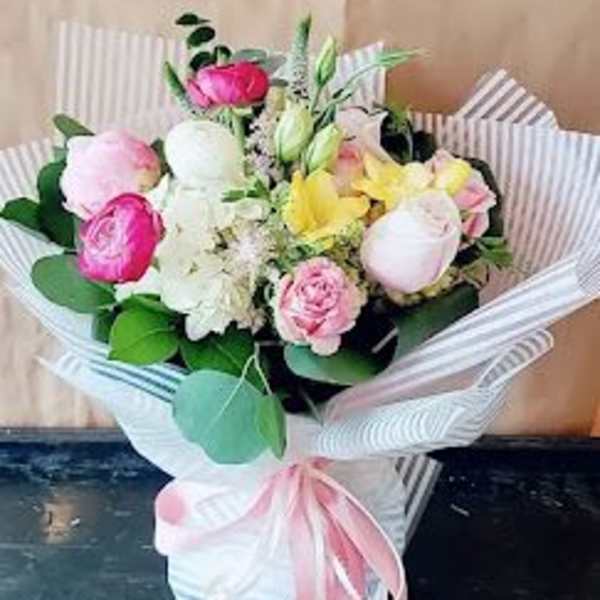 Bouquet of pink, white, and yellow flowers wrapped in striped paper with a pink ribbon