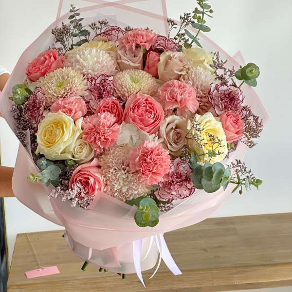Large bouquet of pink, cream, and yellow flowers wrapped in pale pink paper
